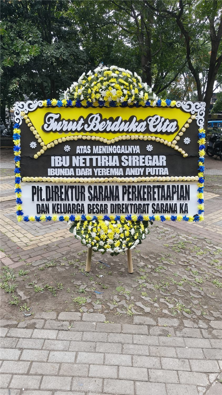 Papan bunga duka cita dengan rangkaian bunga kuning dan putih